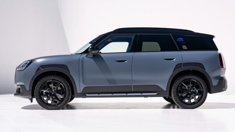 side view of a matte blue Countryman S Untamed parked on a white surface in front of white walls