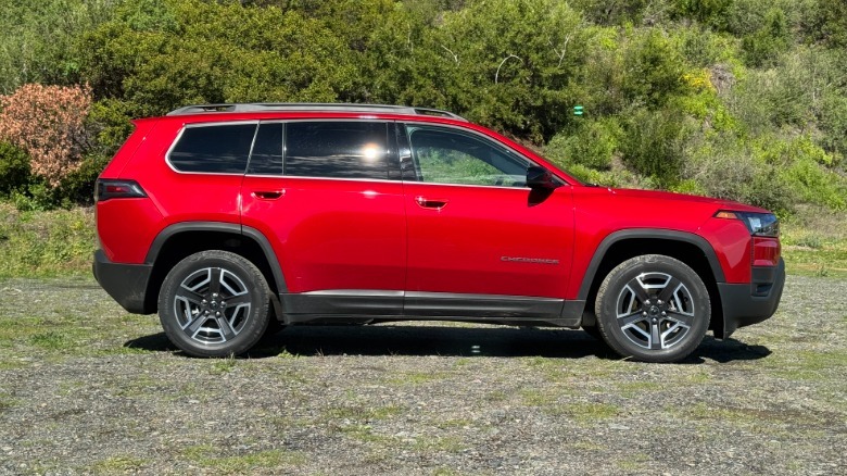 A side view of the red Cherokee parked on gravel in front of bushes