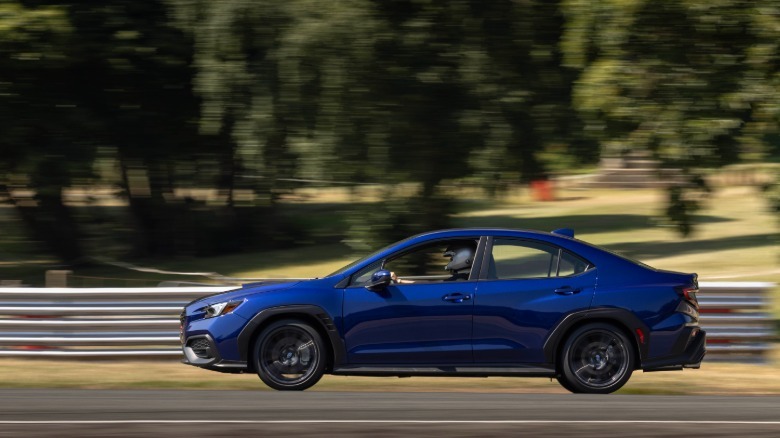 A side view of a blue WRX driving on Oulton Park past trees