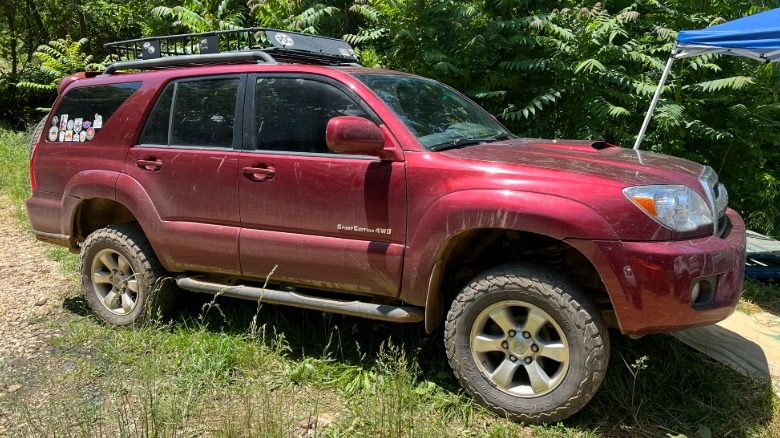 Side view of a red 2006 Toyota 4Runner parked in the grass with trees behind it