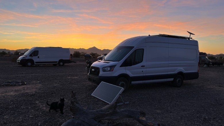 Two camper vans parked in the desert as the sunset turns the sky orange