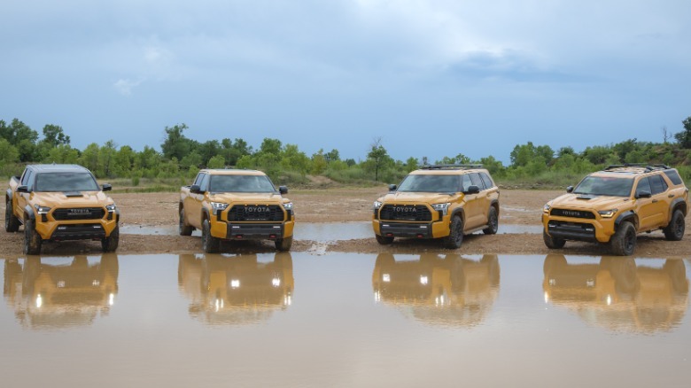 A wide shot of all four TRD Pro models in yellow parked at the edge of a giant mud puddle in front of a cloudy sky