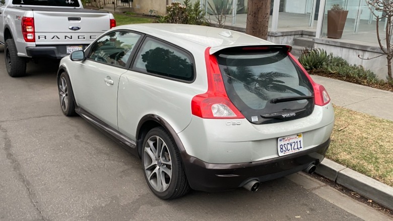 A rear three-quarters shot of a silver Volvo C30 parked next to a curb behind a silver Ford Ranger
