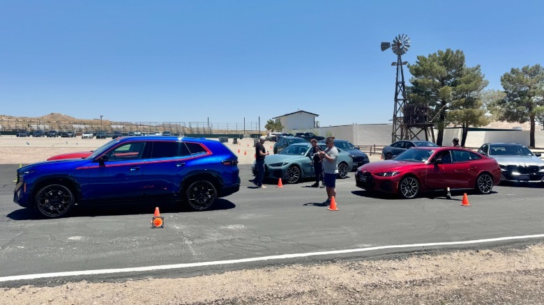 A photo of the drag racing cars lined up in two lanes made of cones inf ront of trees a windmill and desert landscape
