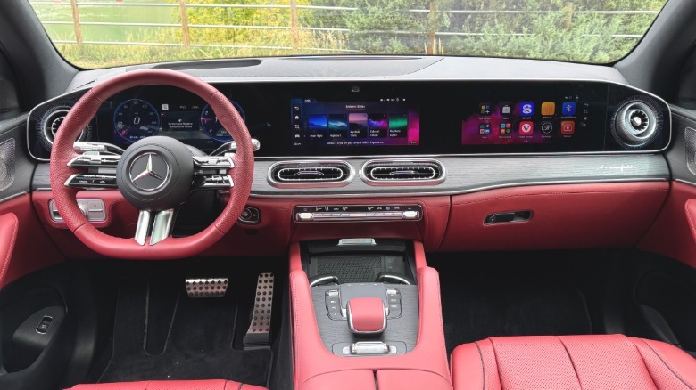 A wide shot of the dashboard in the red interior of the GLE580 with all three screens visible parked with green plants visible out the windshield