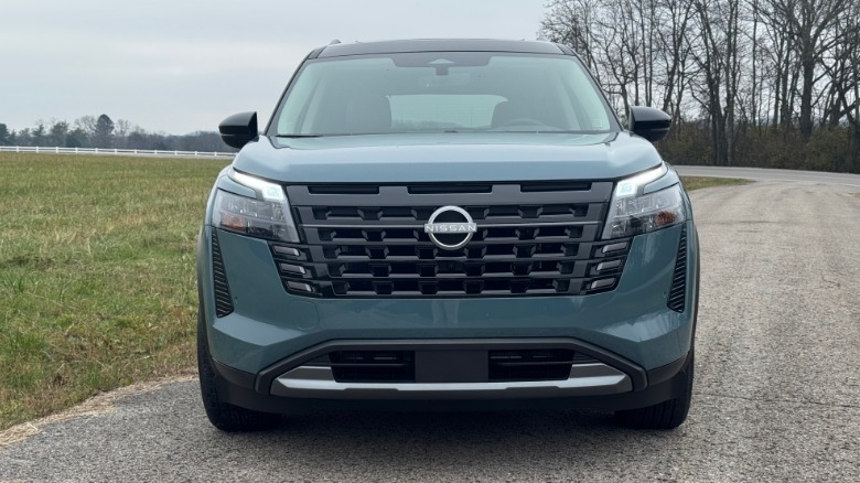 A head-on shot of the teal Pathfinder Platinum parked on asphalt next to grass in front of leafless trees