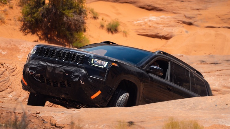 a black Cherokee Trailhawk driving up a steep rock incline with a tree visible behind it