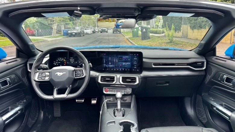 A side shot of the black interior and dashboard in the Mustang EcoBoost with the top down and a residential street visible out the windshield