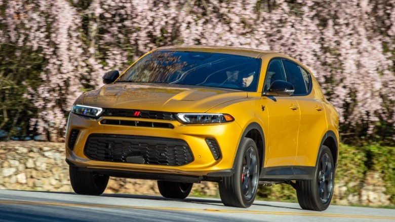 Front three quarters shot of a bright gold Dodge Hornet driving on a road in front of blooming cherry trees