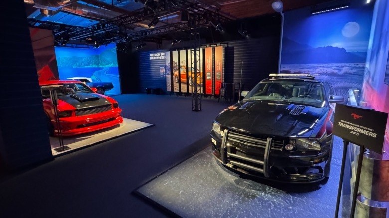 A photo of the movie Mustangs exhibit showing the black Saleen Mustang used in the original Transformers movie and a red Mustang used in the movie Kick Ass