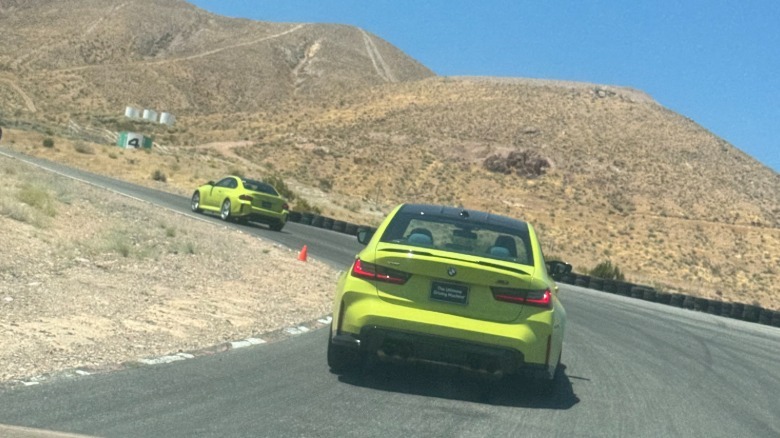 A photo of a highlighter yellow M3 following a highlighter yellow M2 around an uphill corner toward turn four with desert mountains and a blue sky in the background