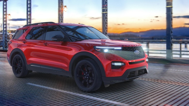 A front three quarters shot of a red 2023 Explorer ST driving across a bridge over water in front of a sunset