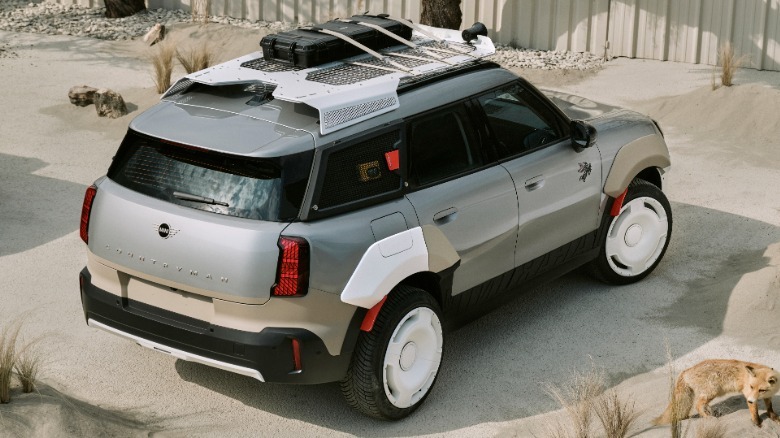 A close-up rear three-quarters shot of the silver Countryman parked on a sandy surface surrounded by shrubs and a fox