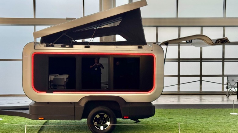 A side shot of the Base Camp trailer with the roof popped and the tailgate open with orange ambient lighting in front of glazed windows