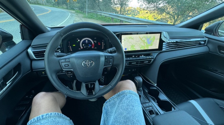 A photo from my POV behind the wheel of the Camry Nightshade with grass and a road visible out the windshield