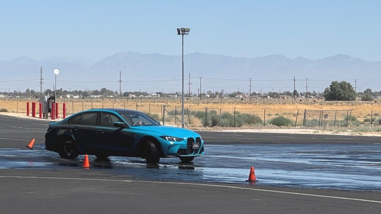 A bright blue M3 sliding on wet asphalt moments after hitting a caution cone and sending it flying