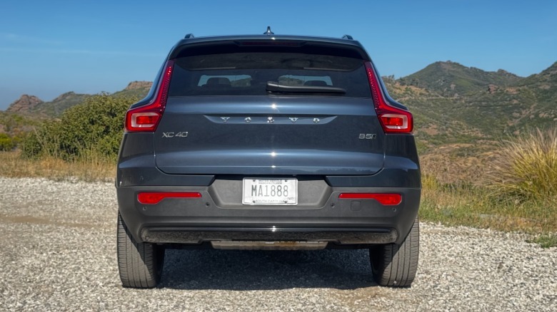 A straight rear shot of the blue XC40 parked on gravel in front of a view of shrub-covered mountains and a blue sky
