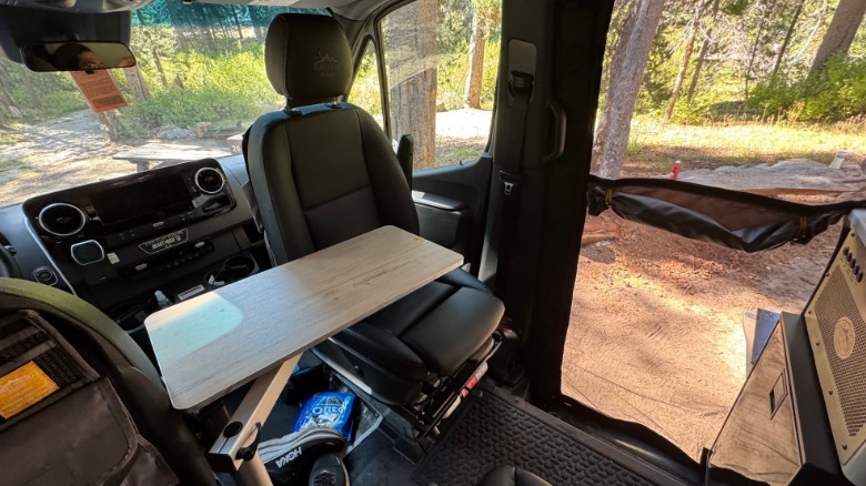 The swiveling passenger seat flipped around with the removable wood table installed with a view of dirt and trees out the windows and open side door