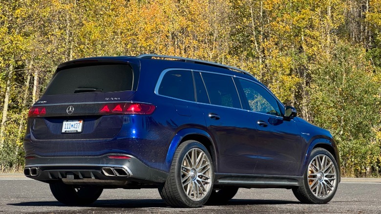 A rear three-quarters shot of my dark blue GLS63 press car parked on asphalt in front of yellow and green trees