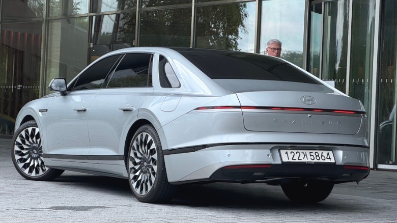 Rear three-quarters shot of a silver Grandeur with someone behind it in front of a wall of windows