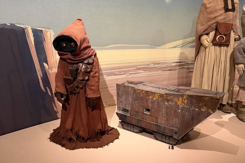 A Jawa costume next to a Jawa Sandcrawler at the Lucas Museum of Narrative Art