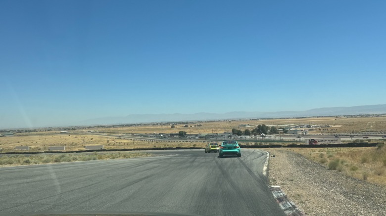A wide shot from the passenger seat showing a turquoise M3 following a highlighter yellow one with the wide view of Willow Springs and the desert and a clear blue sky