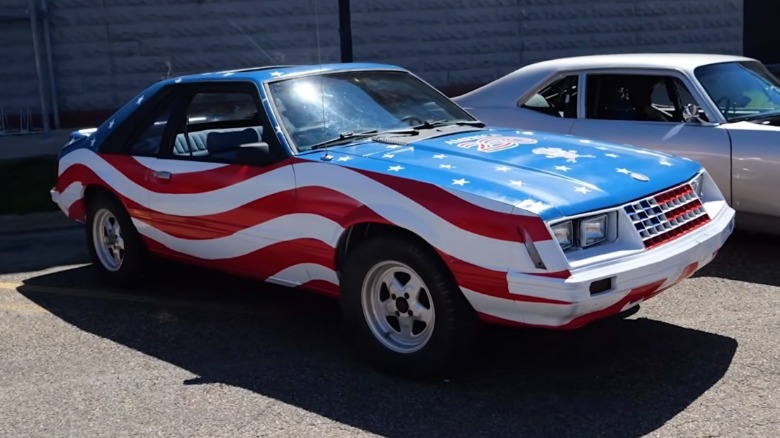 Front 3/4 view of a 1979 Ford Mustang with an American flag paint job parked at a car show