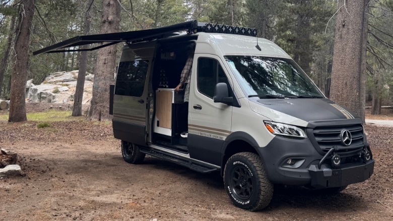 A front three quarters shot of the BeastMode XO with the side awning extended parked on dirt in front of trees and rocks