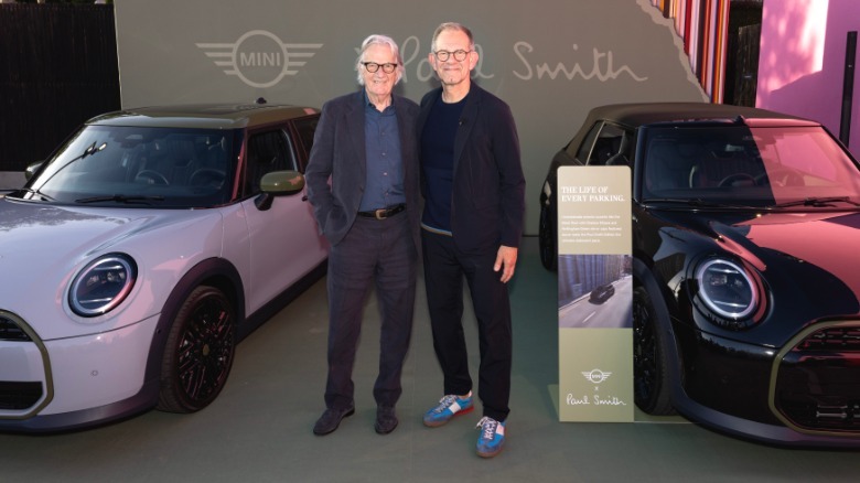 A photo of Holger Hampf and Sir Paul Smith standing between a gray Mini Cooper four-door and a black Mini Cooper Convertible Paul Smith Edition in front of a green Paul Smith sign