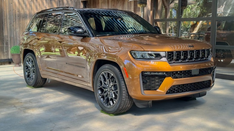 Front three quarters shot of a new Grand Cherokee in the new color of Copper Shino parked on concrete in front of a wood and glass building