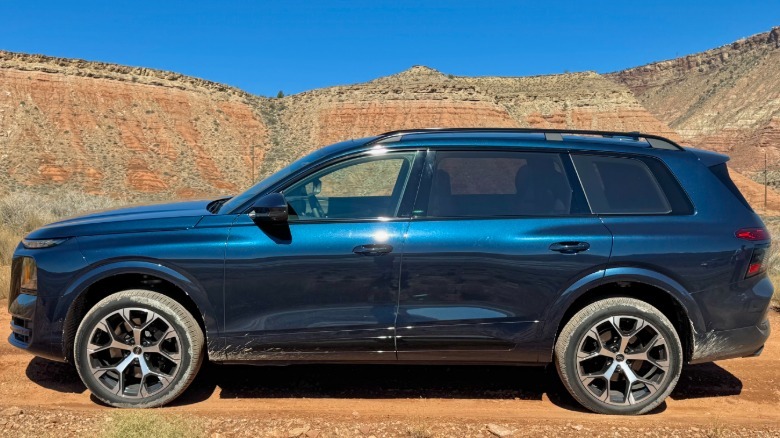 Side view of the dark blue Q9 parked on dirt in front of a blue sky and a mountain range