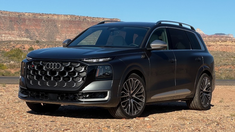 front three-quarters shot of the dark gray SQ9 parked on gravel in front of a blue sky and a mountain