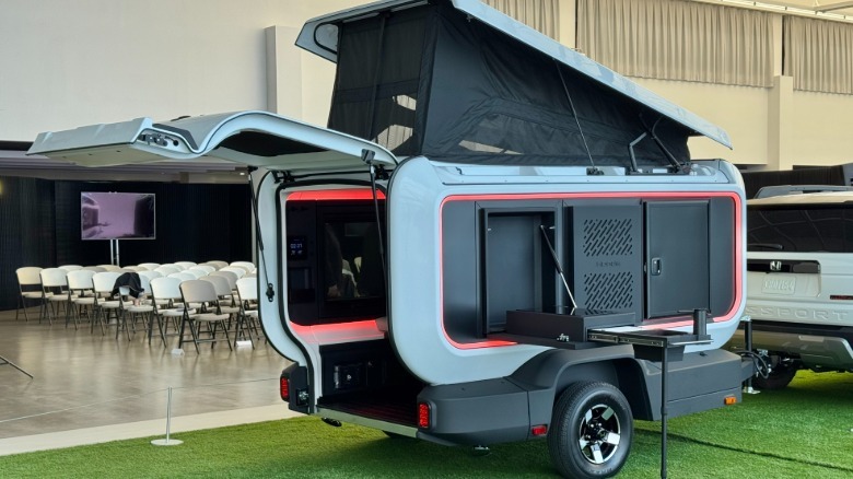 A rear three quarters shot of the Base Camp trailer hitched up to a white Passport TrailSport parked on astroturf with the top popped