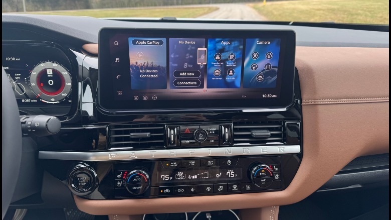 A close-up of the 12.3-inch infotainment screen and the Pathfinder's climate control buttons with grass and a road out the windshield