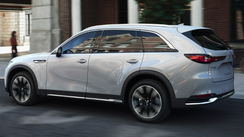rear three-quarters shot of a silver CX-90 driving past a brick building