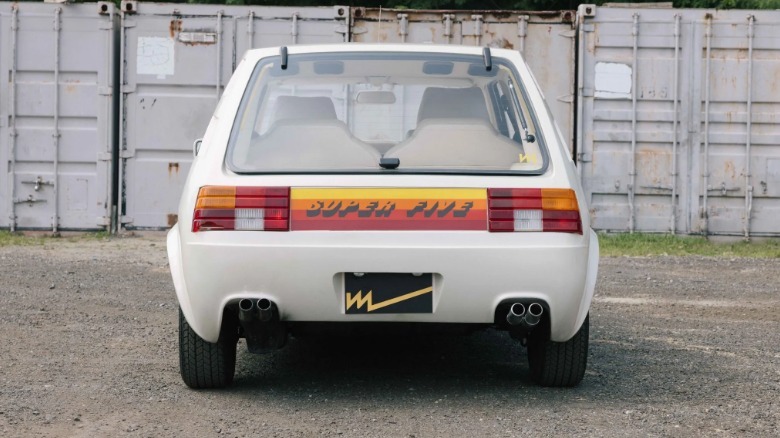 A rear photo of the Super Five showing the red orange and yellow graphic on the rear parked on dirt in front of shipping containers