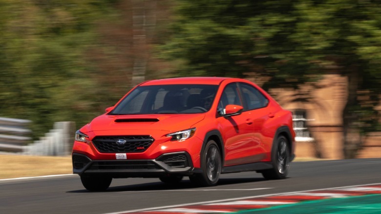 A front three-quarters shot of a red WRX driving on Oulton Park past trees