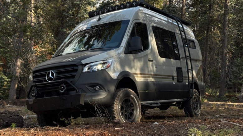 A front three quarters shot of the van parked on mulch in front of trees with its headlights on