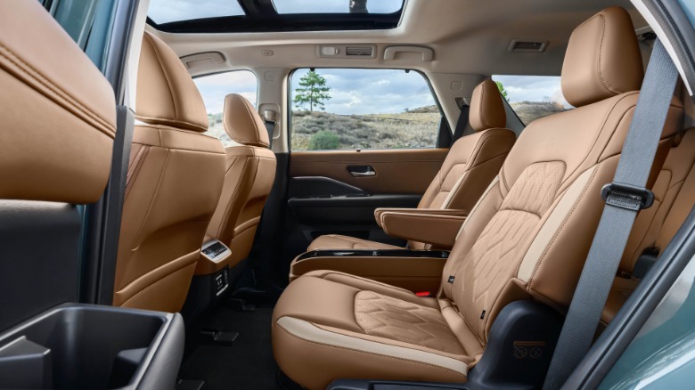 A look in the rear driver's door of a Pathfinder Platinum with brown leather showing the panoramic roof and a tree on a mountian out the window