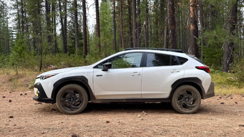 A side shot of the white Crosstrek Hybrid parked on pine needles in front of a bunch of trees