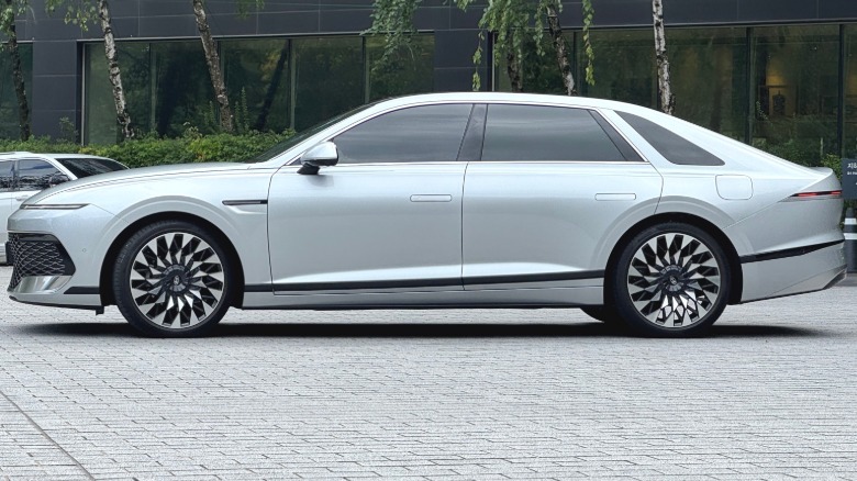 A side view of a silver Grandeur parked on gray brick in front of trees