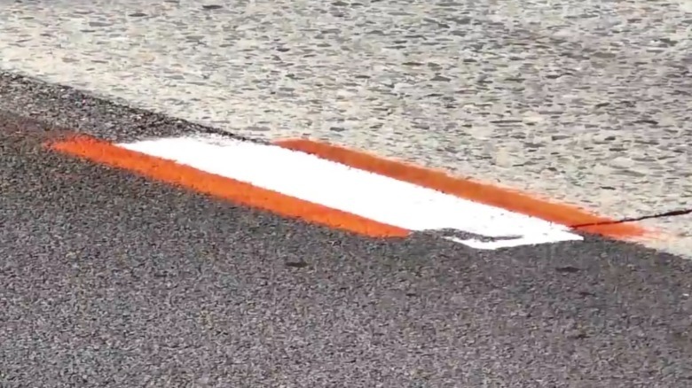A white lane marking with orange markings on either side