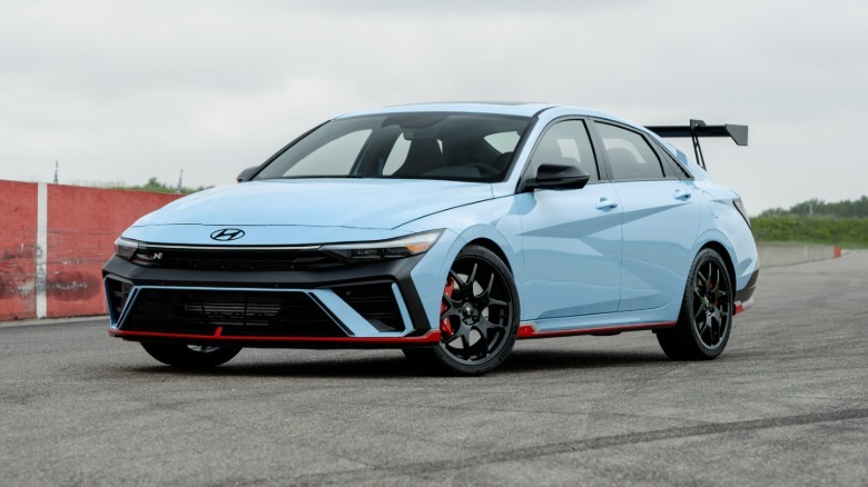 A front three quarters view of a blue Elantra N TCR Edition parked on asphalt in front of a red wall