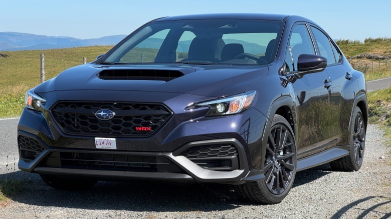 A front three-quarters shot of a Galaxy Purple Pearl WRX parked on gravel next to a road and grass on a clear day