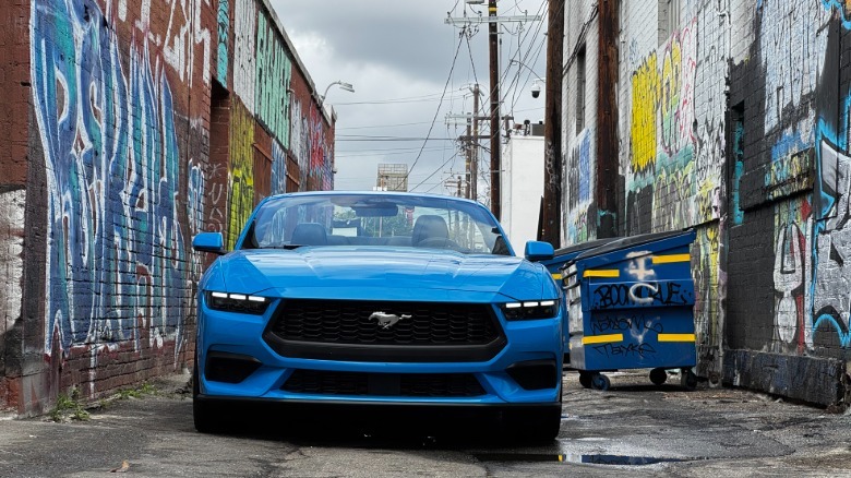 A head-on shot of the bright blue Mustang EcoBoost parked in an alley surrounded by graffiti-covered brick walls and a cloudy sky