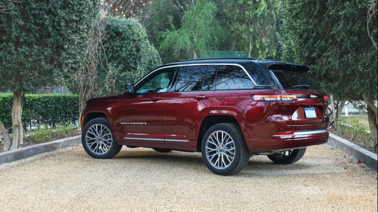 Rear three quarters shot of a burgundy Grand Cherokee parked on dirt between rows of trees