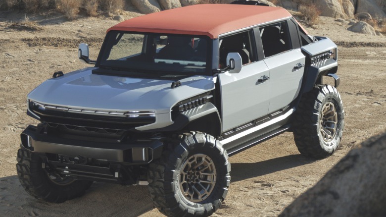 A front three-quarters shot of a white Hummer X SUV parked on dirt in the desert with a red roof