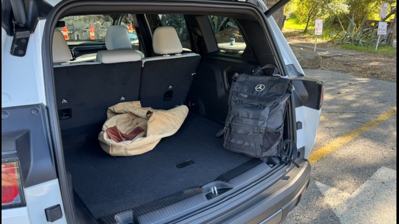 A photo looking into the open trunk of a white Cherokee with a black backpack sitting against the D Pillar and tan coat in the trunk