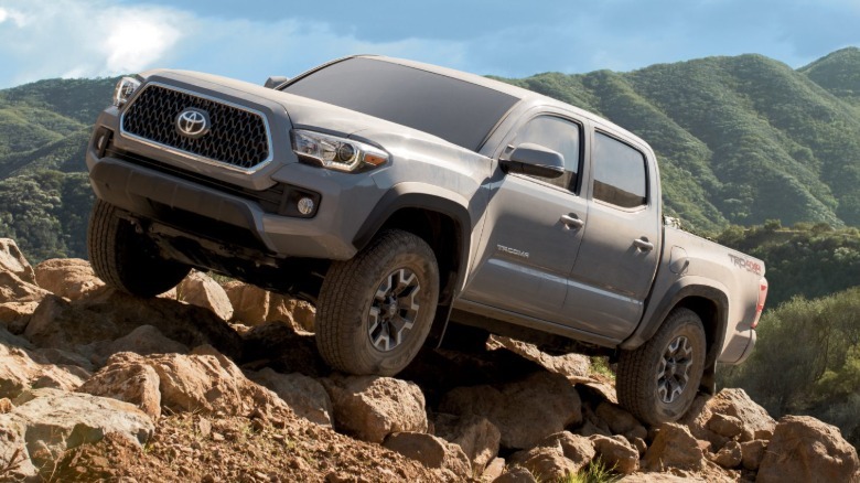 Front 3/4 view of a 2019 Toyota Tacoma climbing rocks with green hills in the background