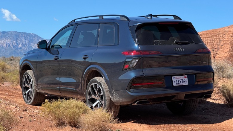 Rear three-quarters shot of the dark blue Q9 parked on a shrubby dirt trail in front of a view of mountains and a blue sky